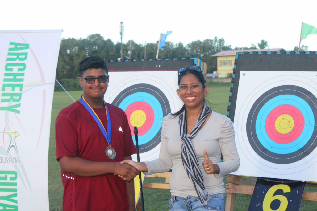 President of Archery Guyana, Ms. Vidushi Persaud-McKinnon on right congratulating Master Saifullah Gani for securing Gold in Men Under 18 Barebow